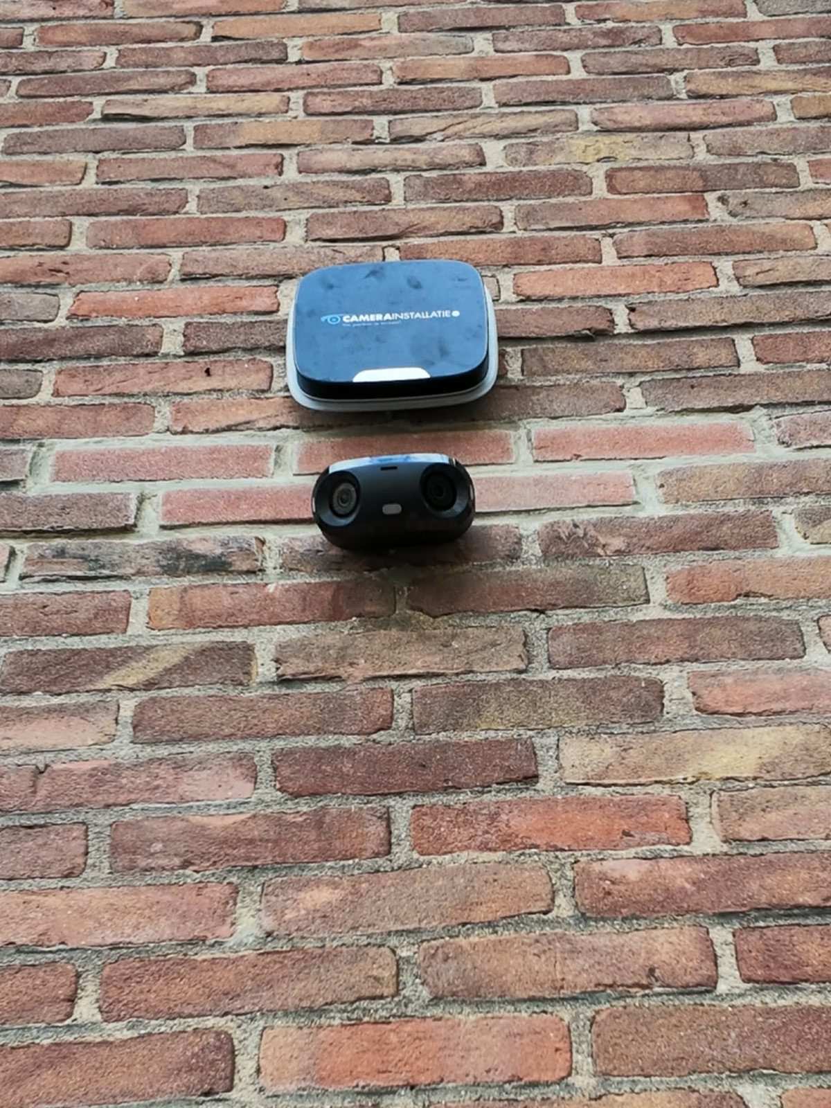 Camera met twee lenzen en een buitensirene samen op een oude gevel