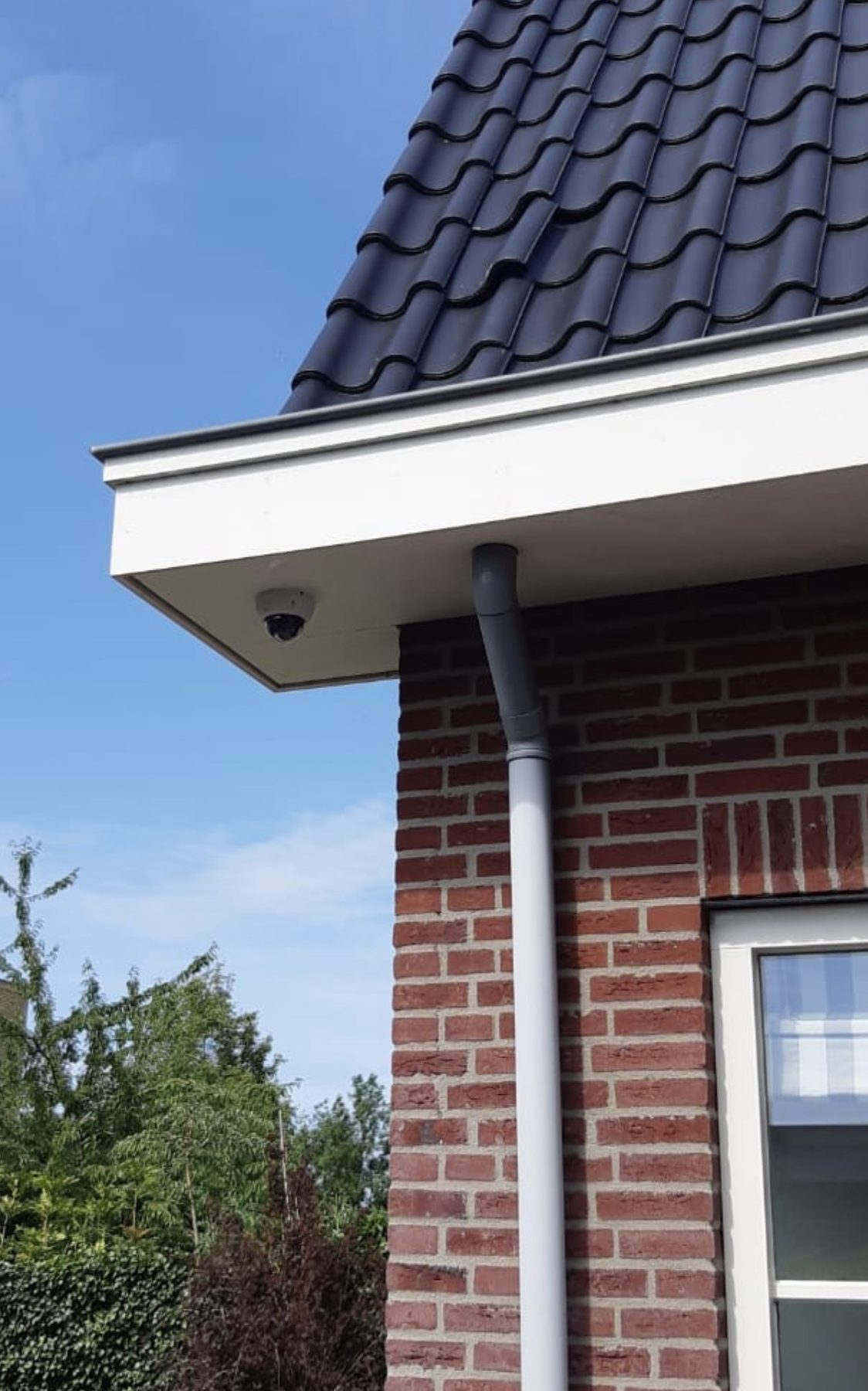 Dome-camera onder een witte dakrand van een woning met rode baksteen
