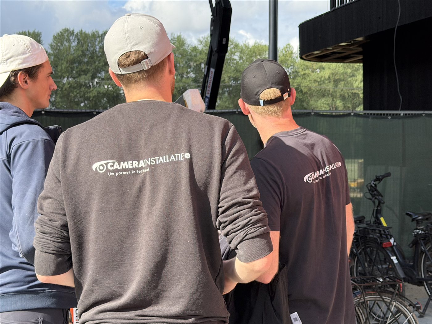 Drie monteurs in bedrijfskleding van CameraInstallatie overleggen op locatie