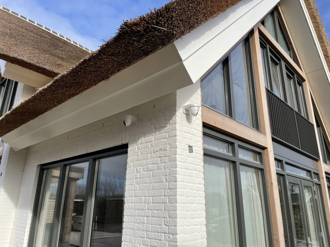 Kleine dome-camera onder de dakrand van een villa met rieten kap en witte gevel