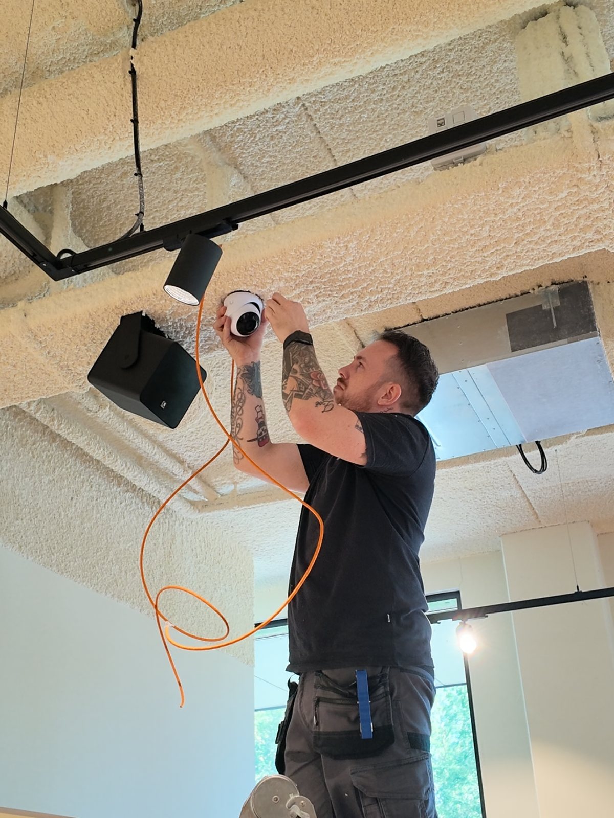 Monteur monteert een dome-camera aan het plafond, met oranje netwerkkabel