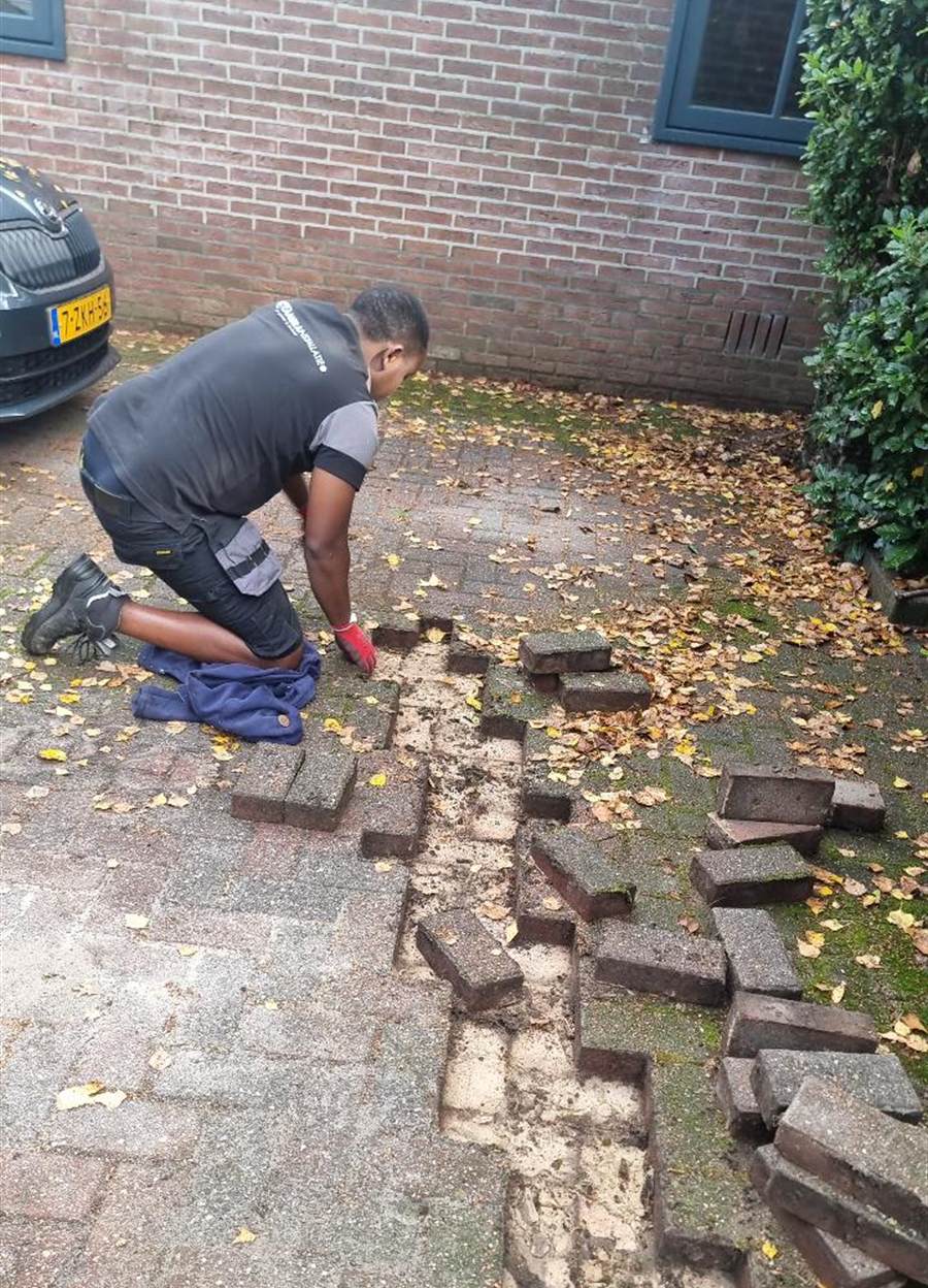 Monteur legt de bestrating van een oprit open om de netwerkkabel eronder door te leggen.