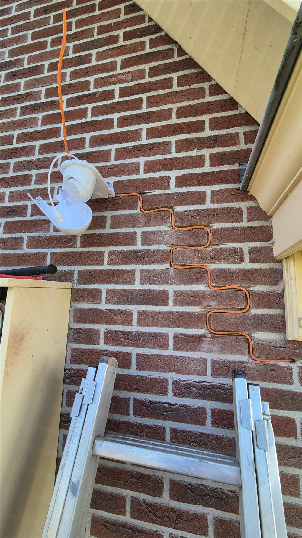 Oranje netwerkkabel netjes weggefreesd in het voegwerk naar een camerapositie