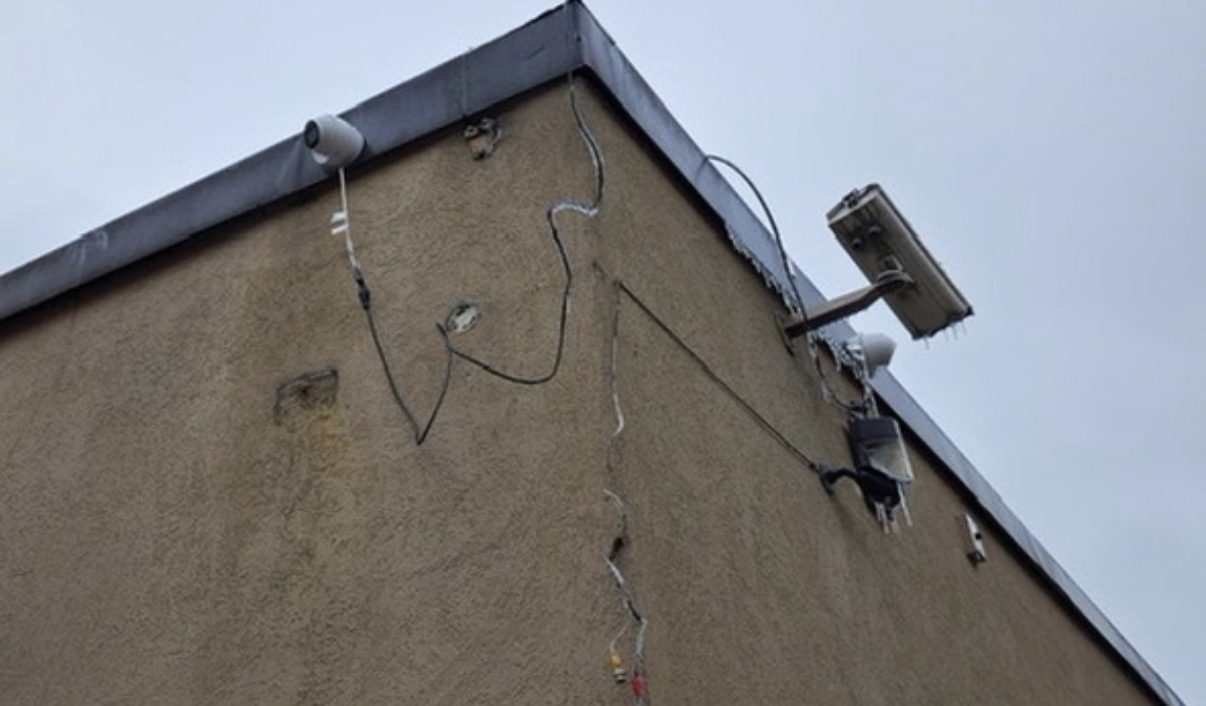 Slecht geplaatste camera met loshangende kabels langs een gevel