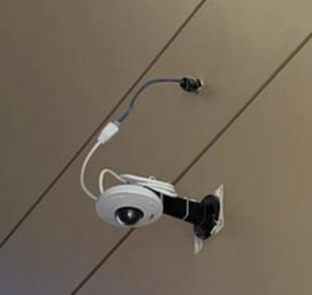 Dome-camera aan een plafond met zichtbare stekker en kabellus