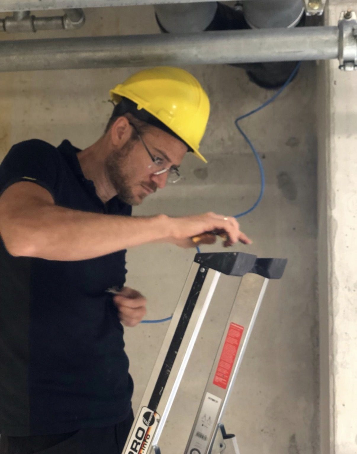 Specialist John trekt bekabeling weg onder een betonnen plafond