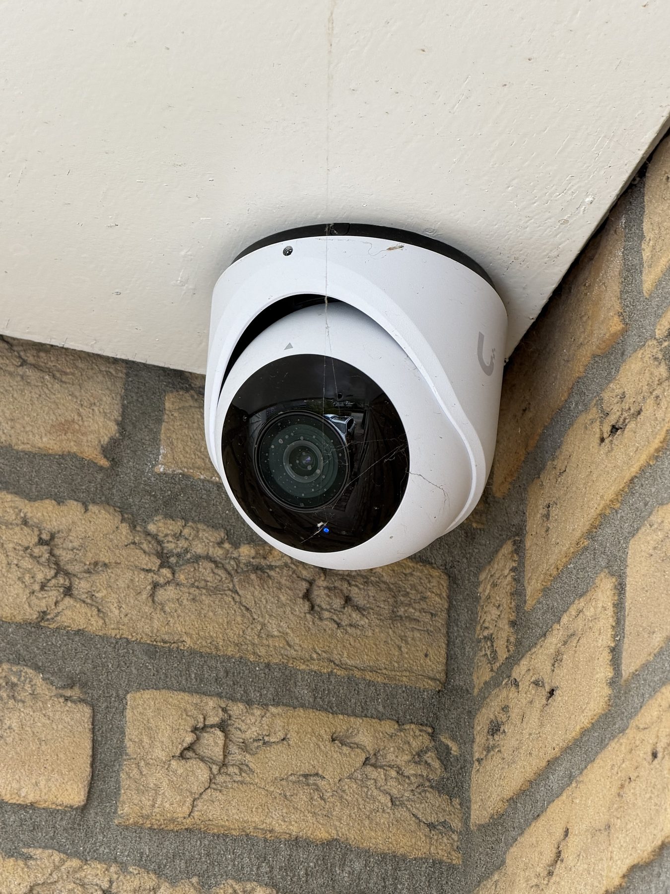 Witte turret-camera strak tegen een gemetselde gevel, geen kabel zichtbaar