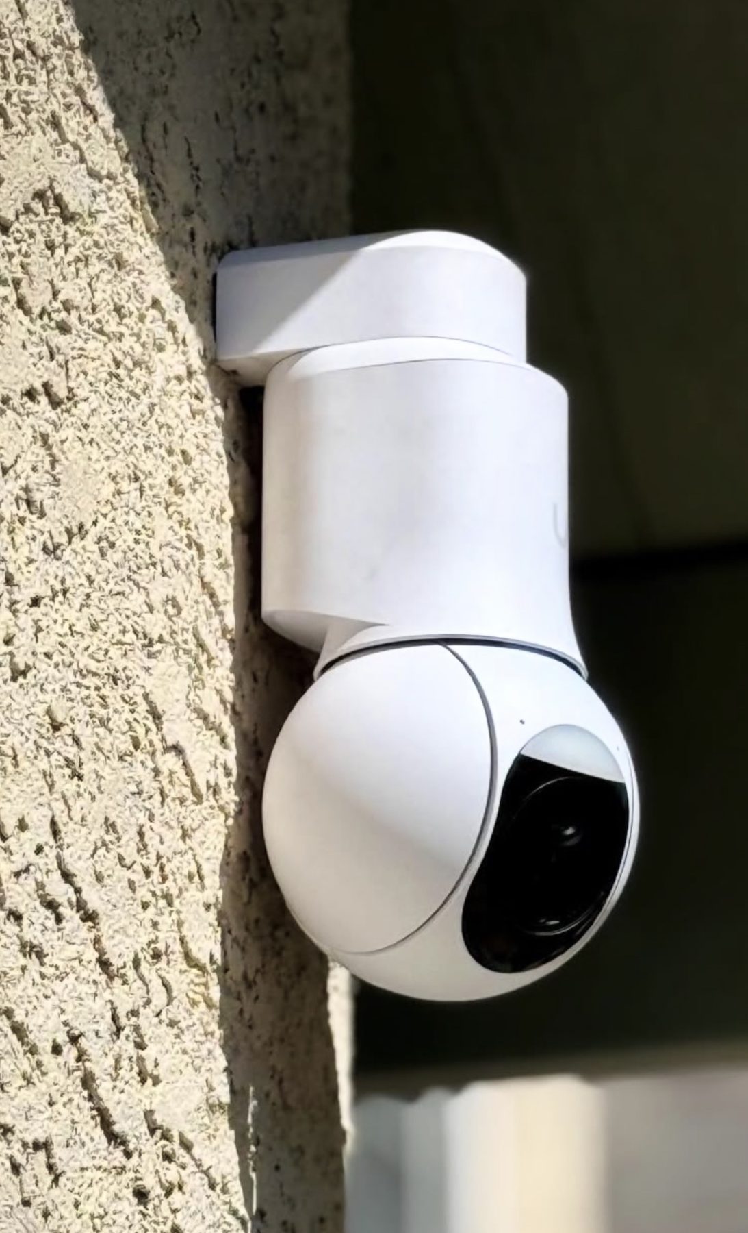 Witte PTZ-camera die kan draaien en zoomen, op een gestucte muur