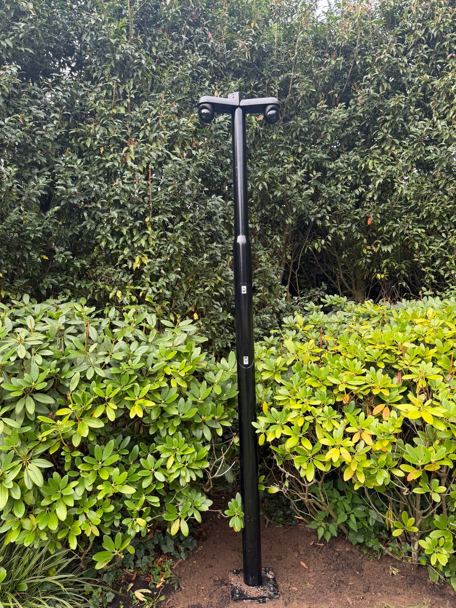 Camera met twee lenzen op een paal in de tuin, de kabel weggewerkt door de paal