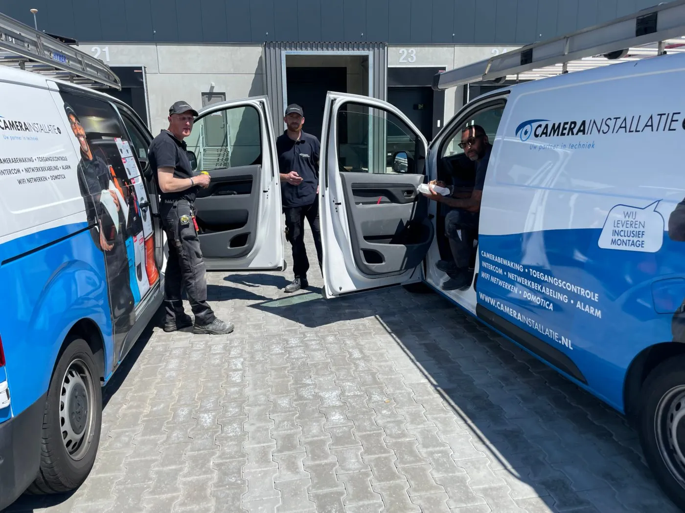 Drie monteurs bij twee bedrijfsbussen met open deuren op locatie