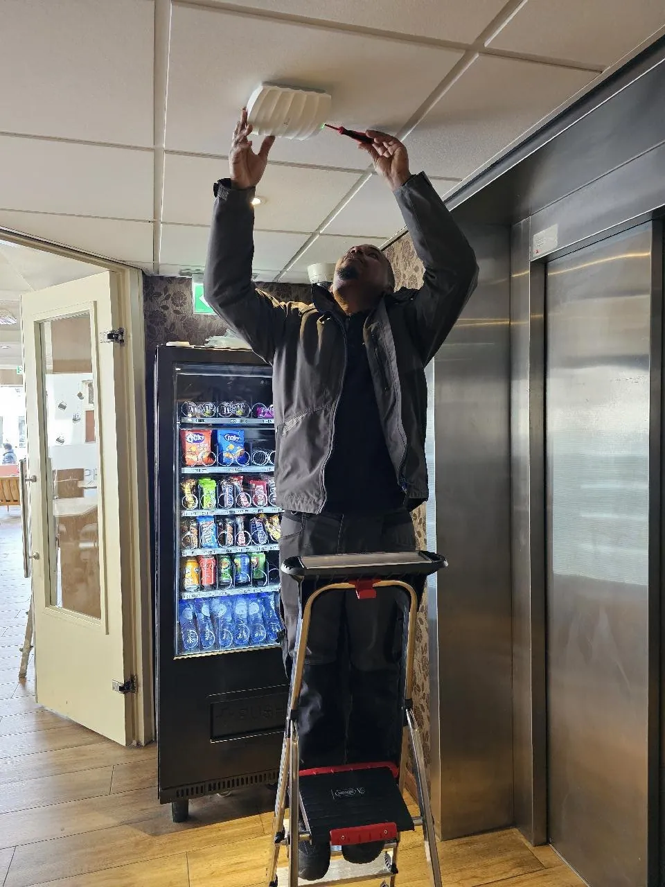 Monteur vanaf een trap plaatst een access point in de hotellobby in Amsterdam