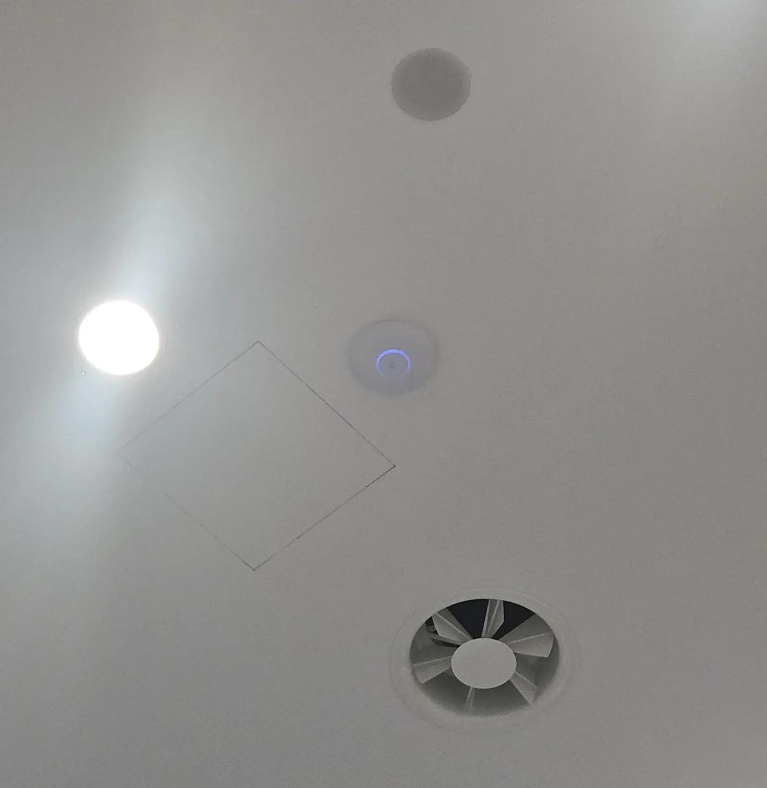 Wit rond access point aan een kantoorplafond in Amsterdam, tussen spot, luik en luidspreker