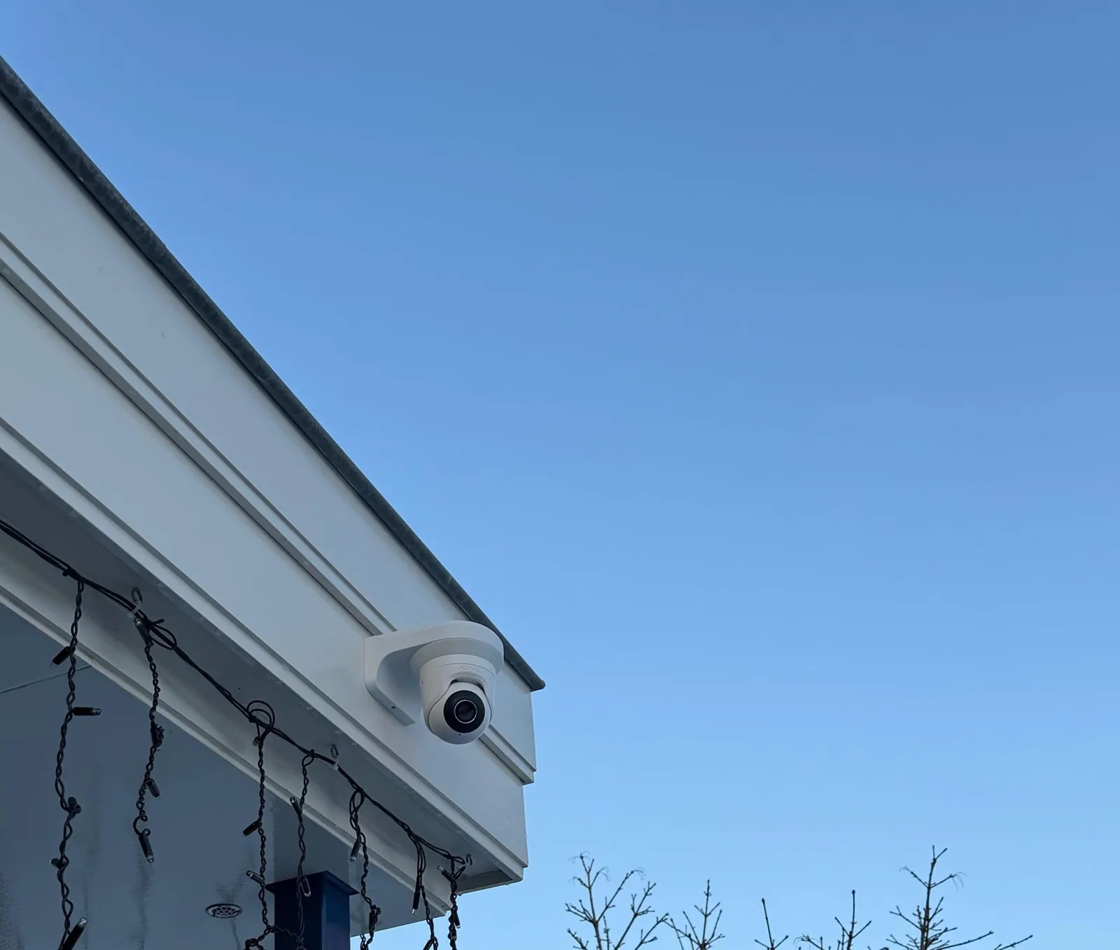 Witte Ajax-camera op de hoek van een witte dakrand bij een woning in Oudewater, tegen een blauwe winterlucht