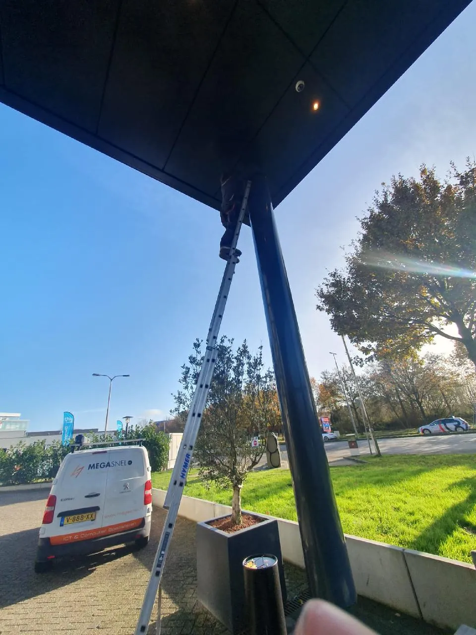 Monteur op een ladder monteert een camera onder de entreeluifel van het hotel in Hoorn