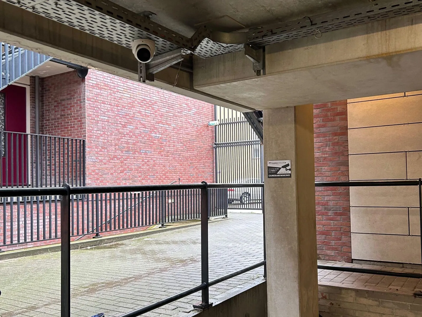 Bulletcamera onder het betonnen parkeerdek van een complex in Amsterdam, gericht op het binnenterrein