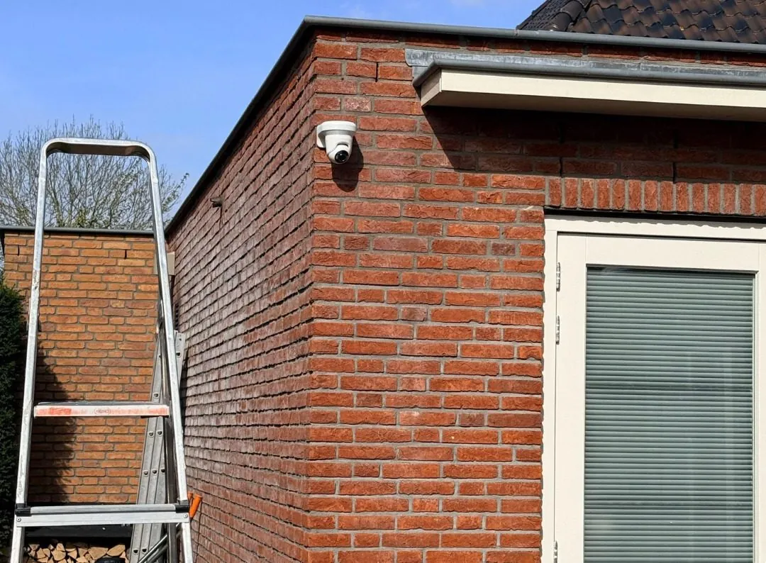 Bewakingscamera hoog op de bakstenen hoek van een woning, tijdens de montage