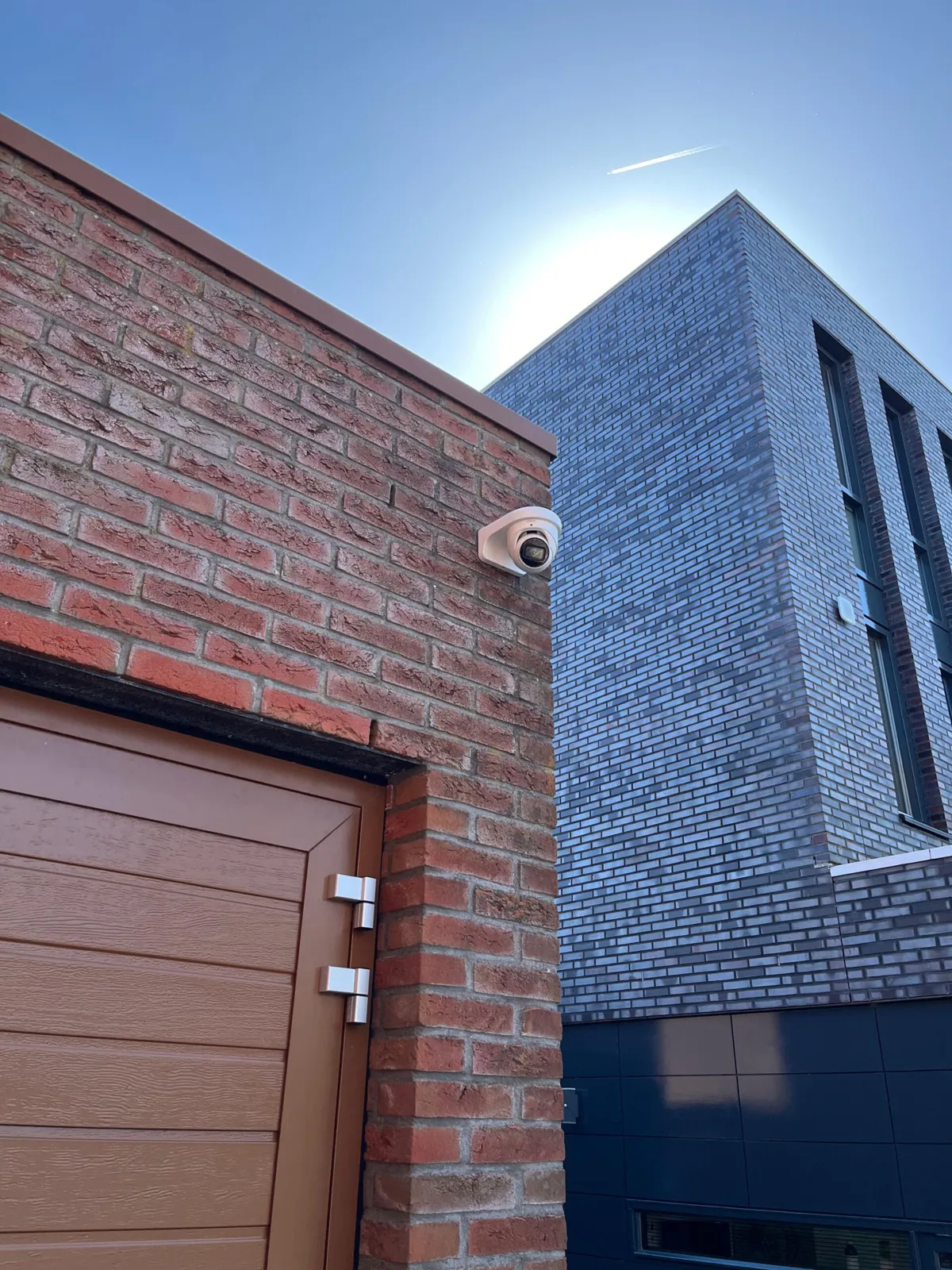 Witte camera op de hoek boven een garagedeur in Almere, met strakblauwe lucht