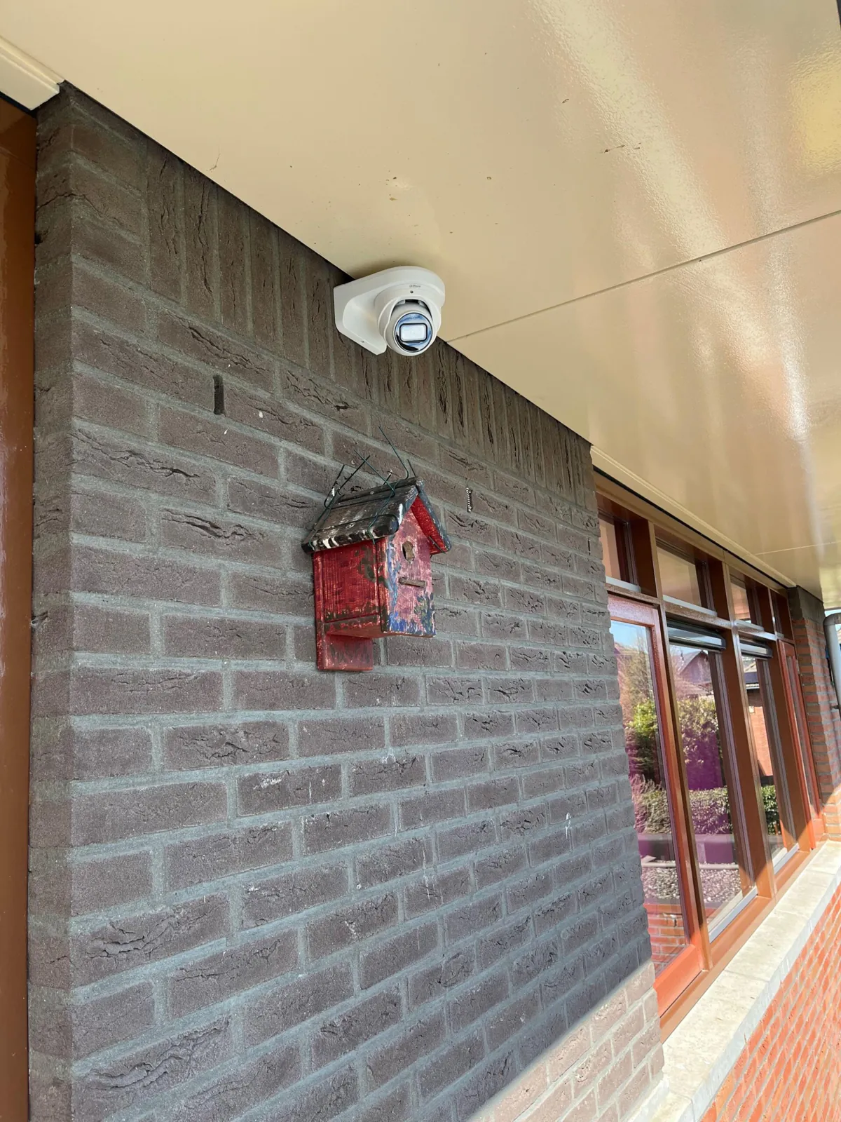 Compacte camera onder een licht plafond tegen een donkere gevel in Almere, boven een rood object