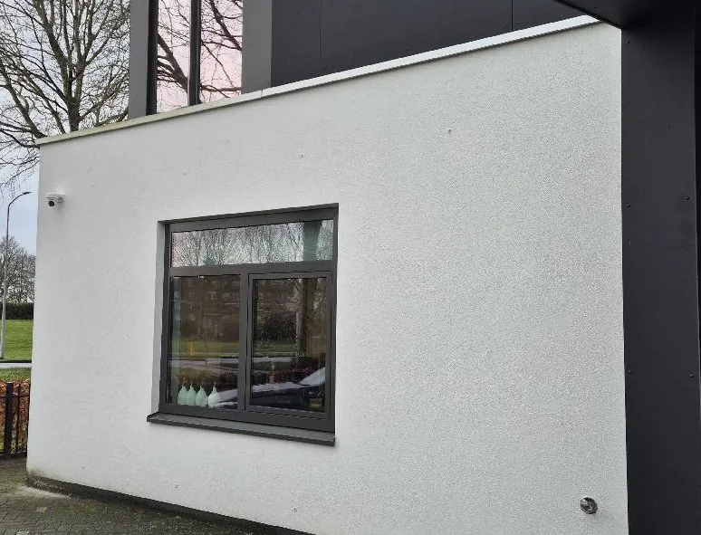 Witte aanbouw in Almere met een raam en een compacte camera bij de dakhoek