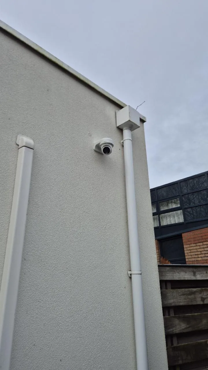 Witte camera tussen twee regenpijpen op de lichte gevel van een woning in Almere