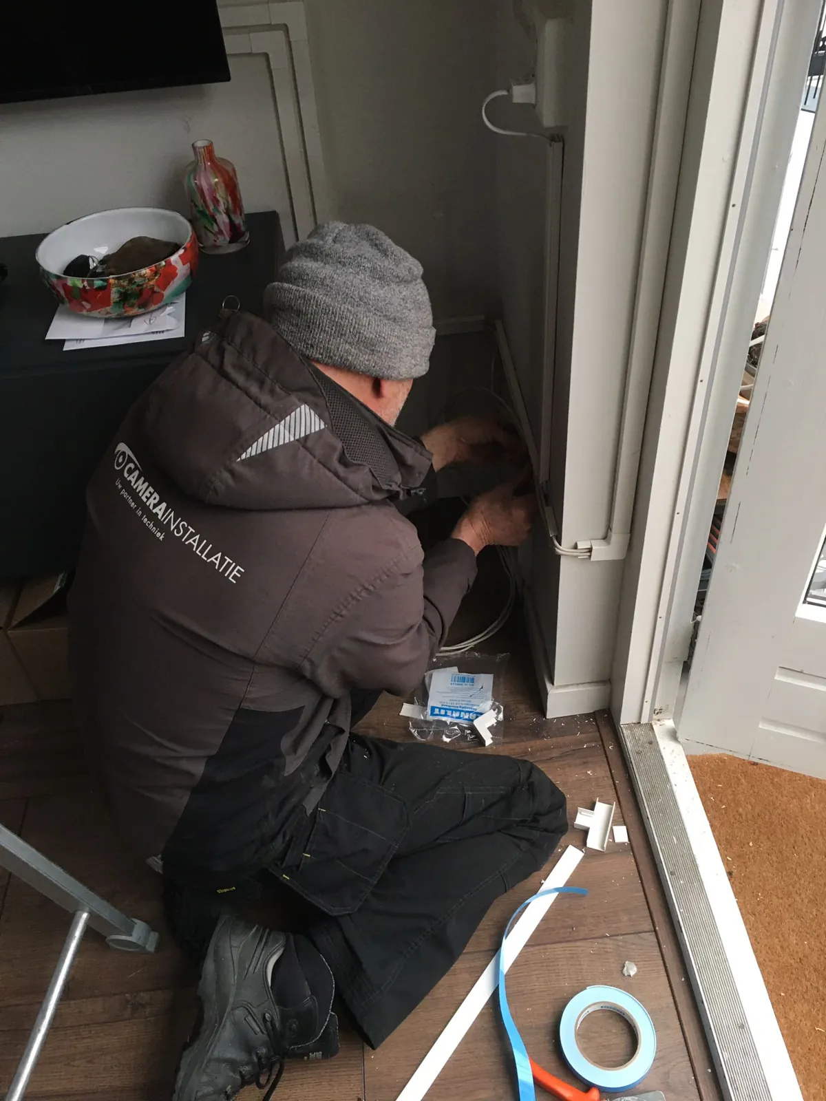 Monteur geknield bij de deurpost werkt aan de camerakabel in een chalet in Biddinghuizen
