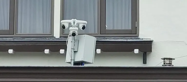 Twee witte camera's en een grijze kast hoog op een gebouw in Blaricum