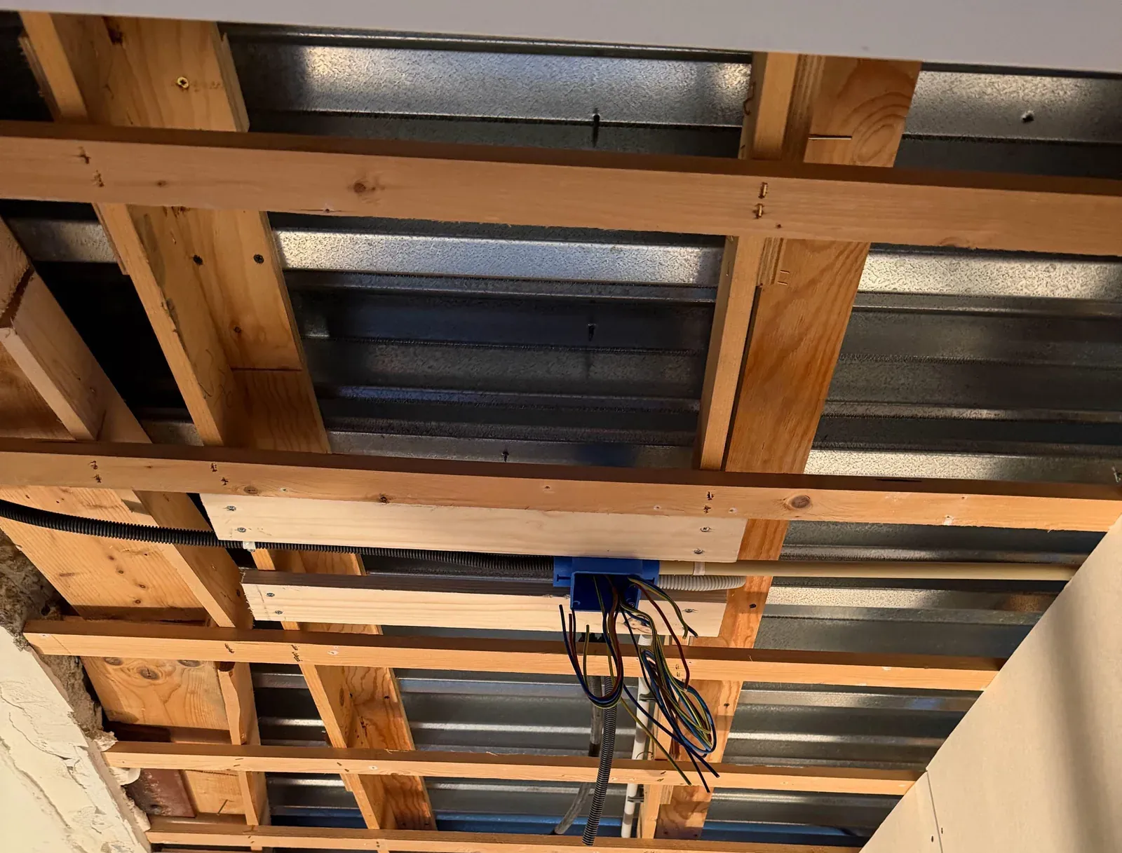 Blauwe centraaldoos met flexbuis tussen de regels van het open plafond in Almere