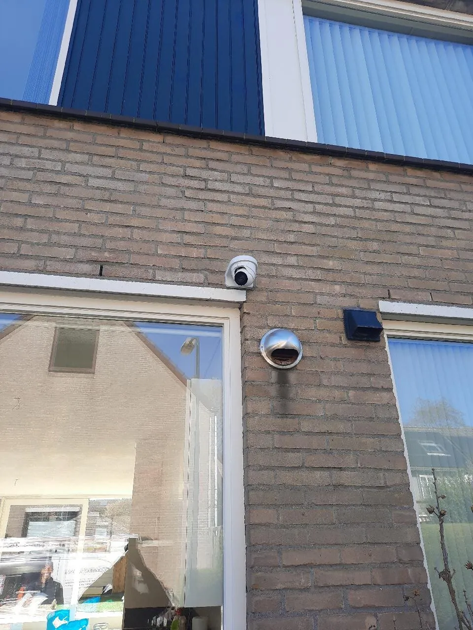 Witte Dahua-camera op de bakstenen gevel boven de schuifpui van een woning in Leidschendam