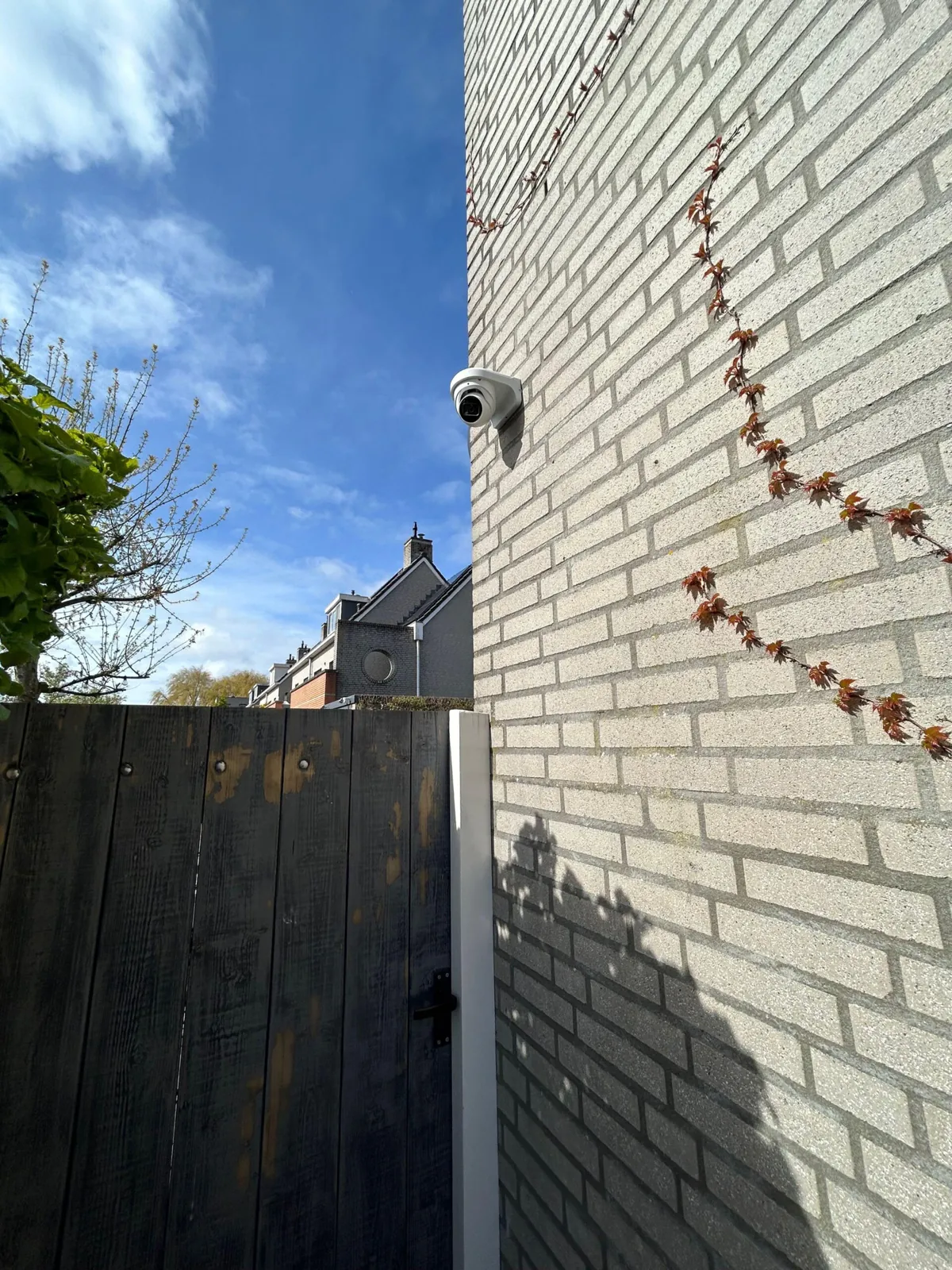 Witte Dahua-camera op de zijgevel van een woning in Hoofddorp, met een houten tuinpoort ernaast