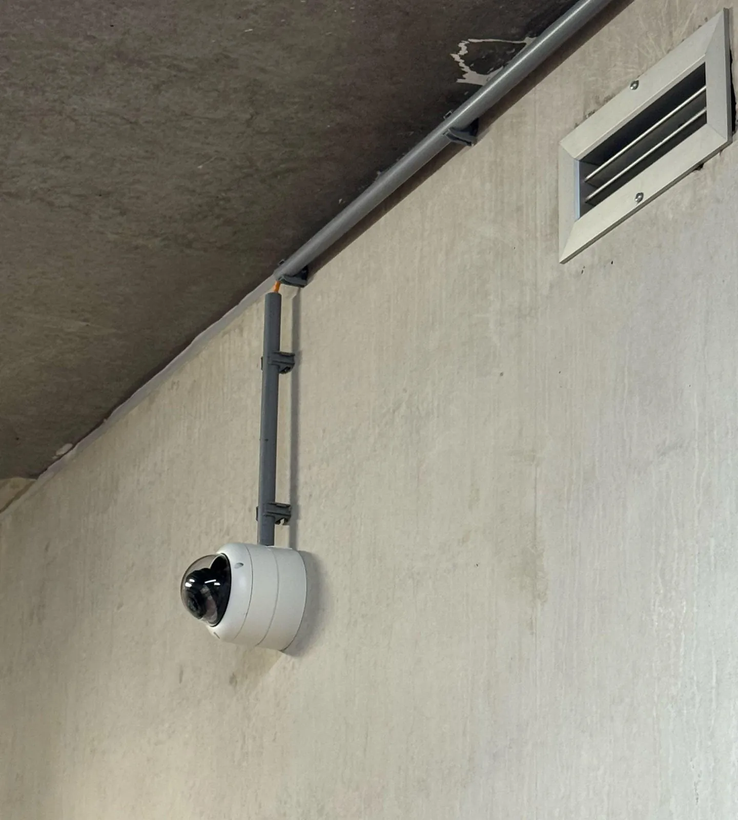 Witte Dahua-dome op een betonnen muur in Born, kabel in een pvc-buis naar boven