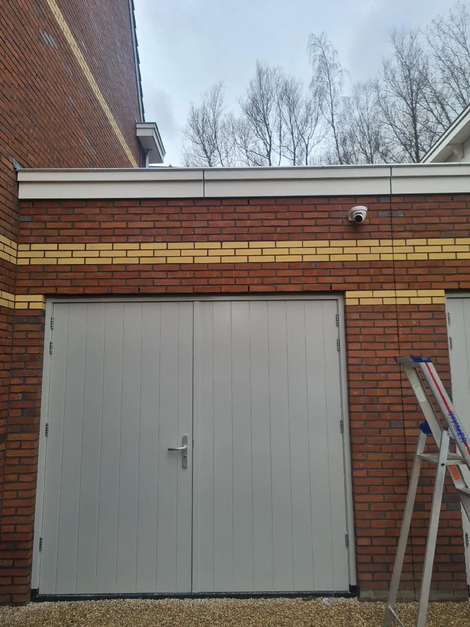 Witte dome-camera onder de dakrand boven de garagedeuren van een vrijstaande woning in Leidschendam