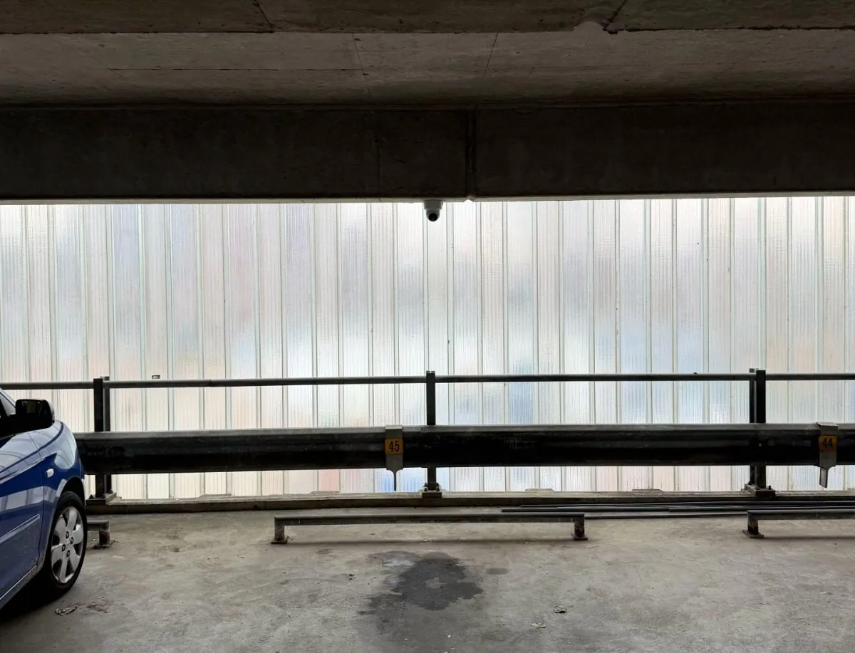 Dome onder een betonnen balk boven een parkeervak, bij een gevel met genummerde plaatsen