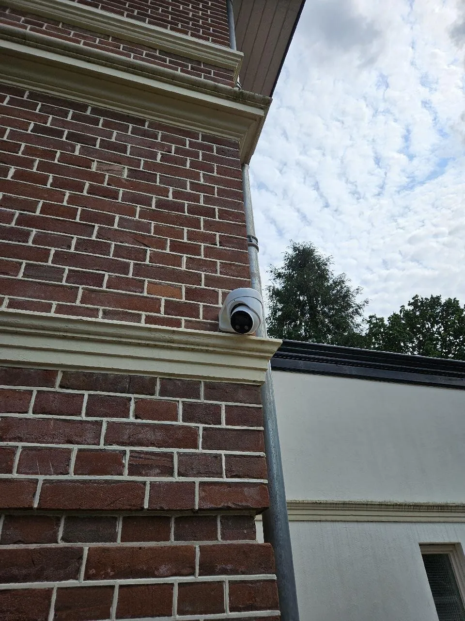 Witte dome-camera op een bakstenen gevel naast de regenpijp, zonder kabel in zicht