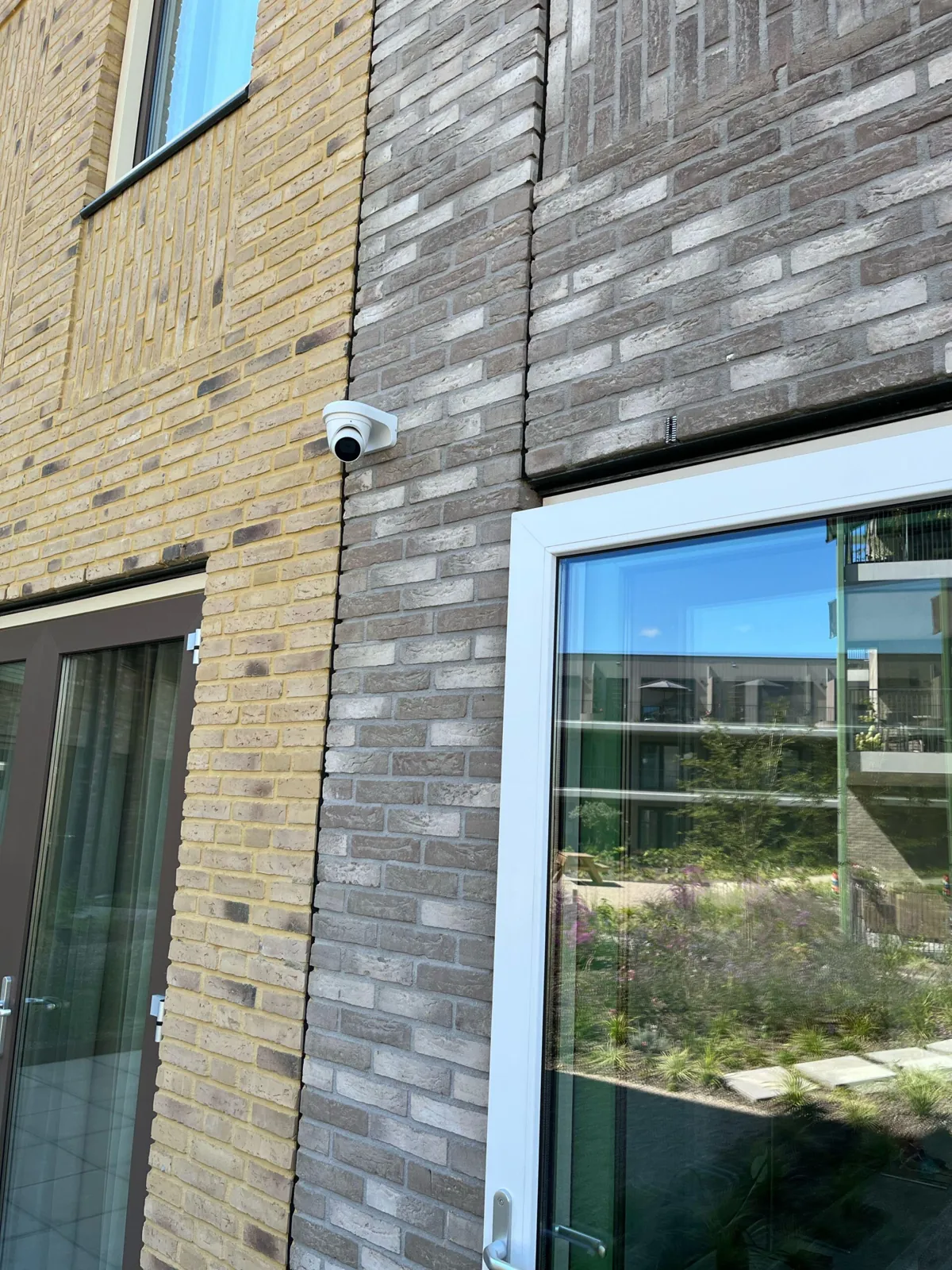 Witte dome IP-camera aan een bakstenen gevel naast een grote tuindeur