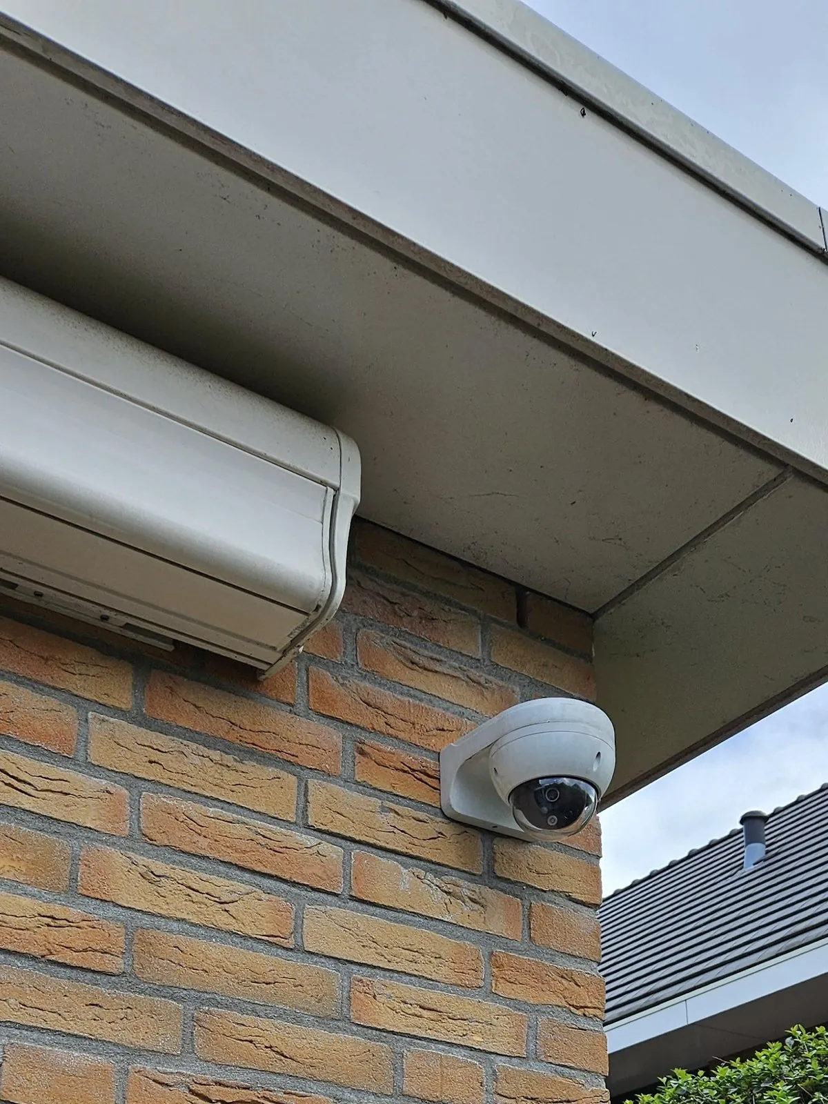 Witte domecamera op de hoek van een gevel in Zoetermeer, onder de dakrand naast een zonnescherm