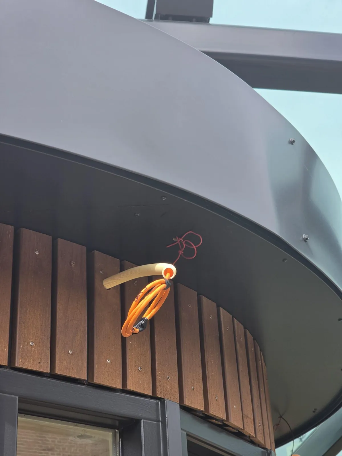 Opgerolde oranje kabel in een buis bij de dakrand in Oss, wachtend op de camera