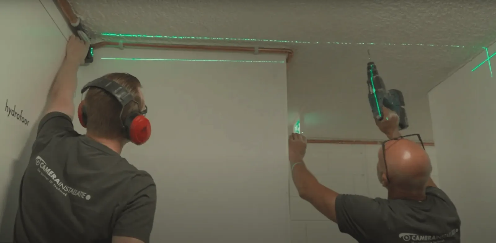 Twee monteurs hangen een kabelgoot langs het plafond recht met een groene laser, Haarlem