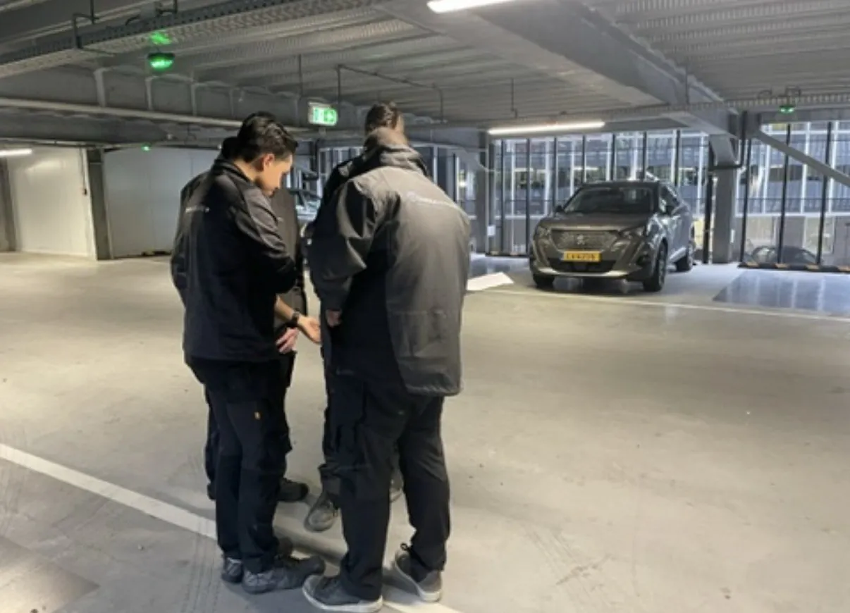 Monteurs stemmen op de garagevloer met het schema af waar elke kabel heen gaat, Amsterdam