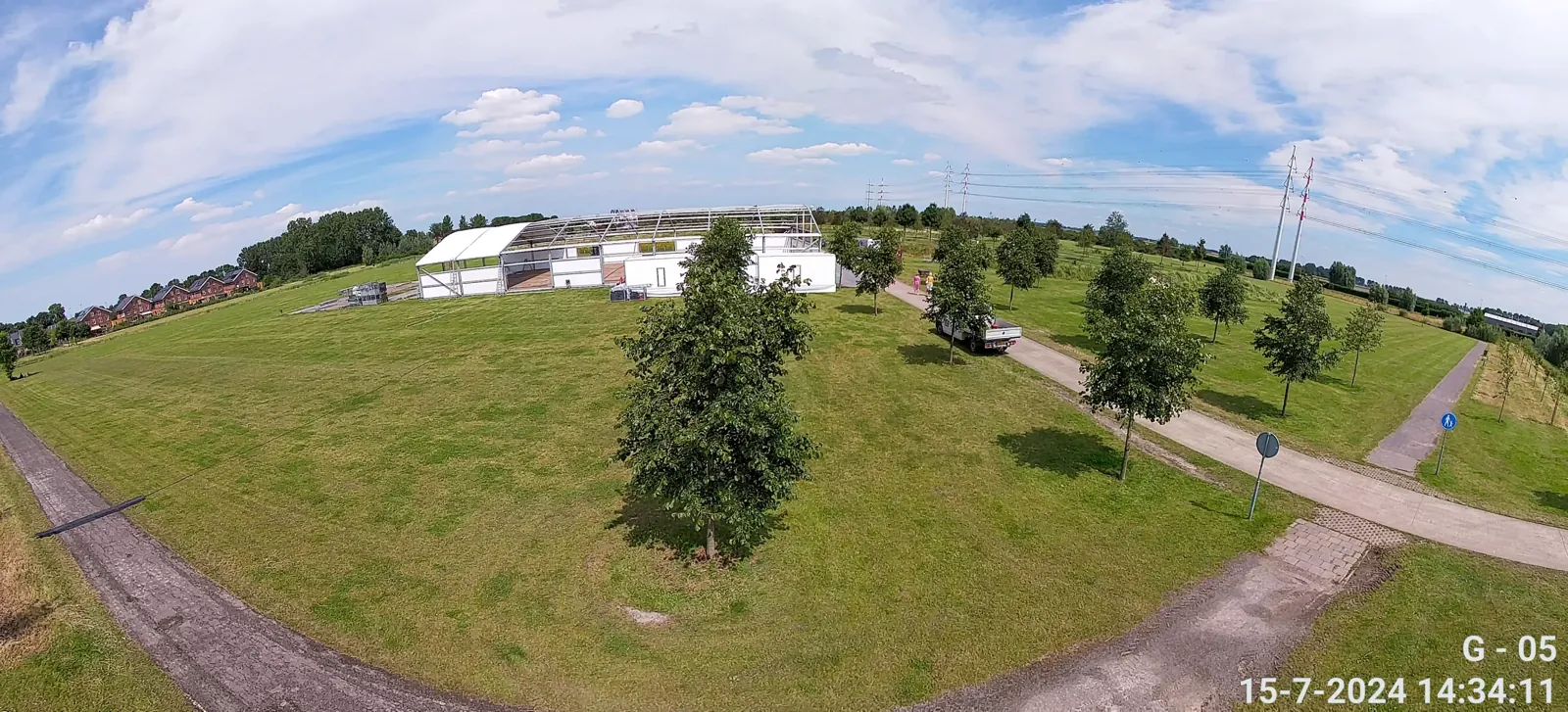 Overzichtsbeeld vanaf de mast op een evenementterrein met grasveld, tent en bomen
