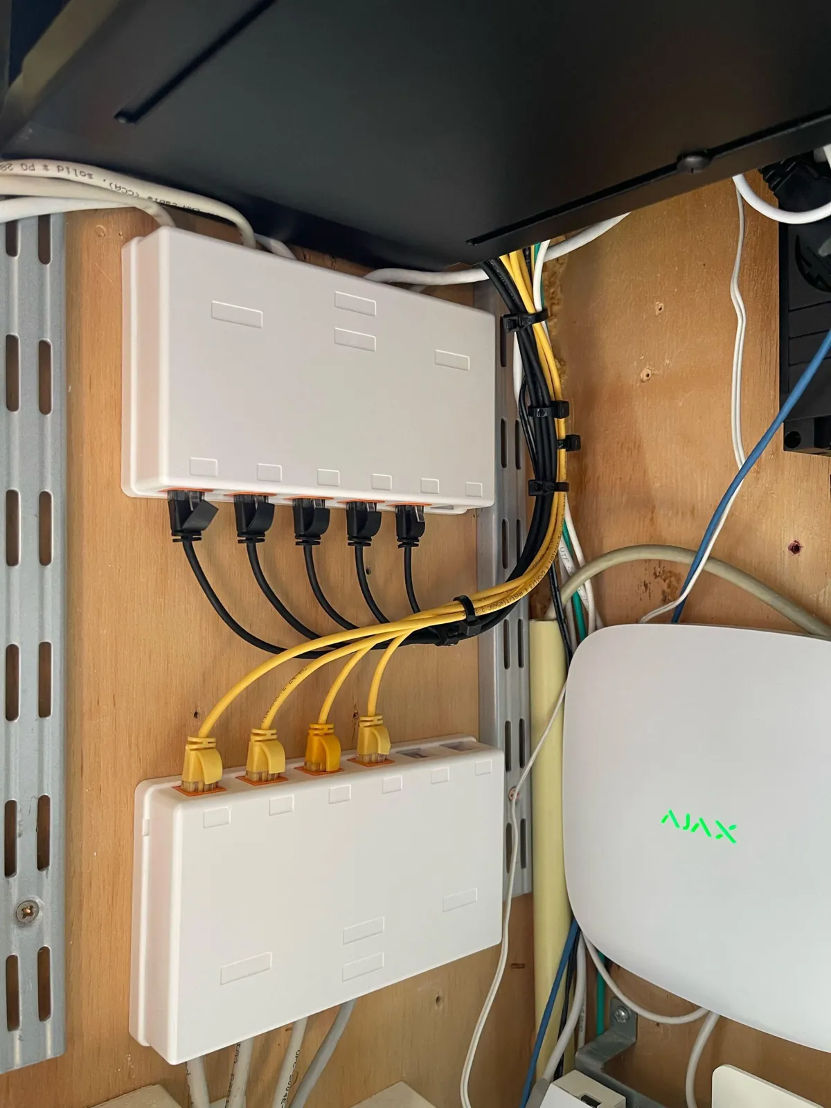 Meterkast met witte patchpanelen, gele en zwarte patchkabels en een Ajax Hub