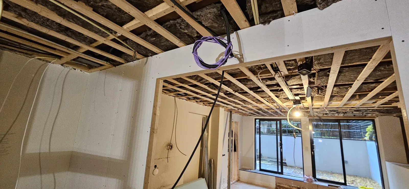 Paarse netwerkkabel en zwarte flexbuis in een open balkenplafond tijdens de verbouwing in Amsterdam