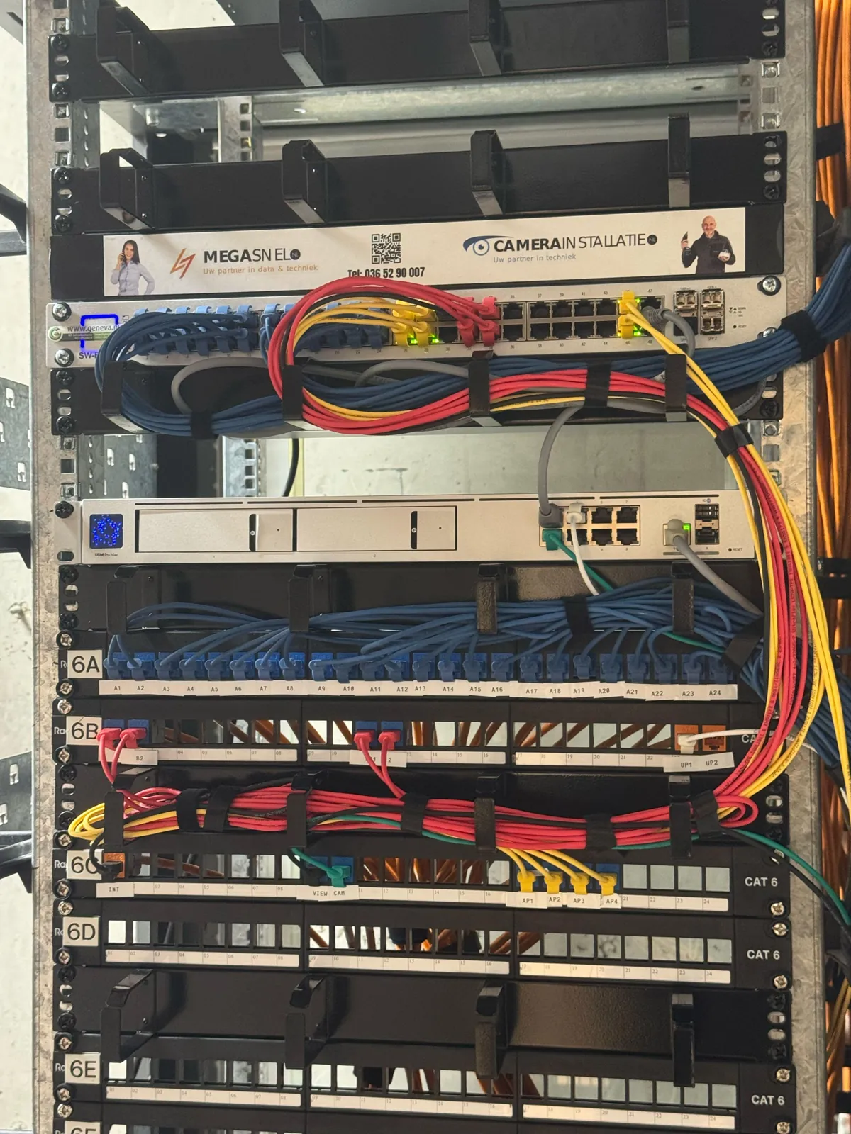 Netwerkkast met UniFi-gateway, managed switch en genummerde patchpanelen in een bedrijfspand