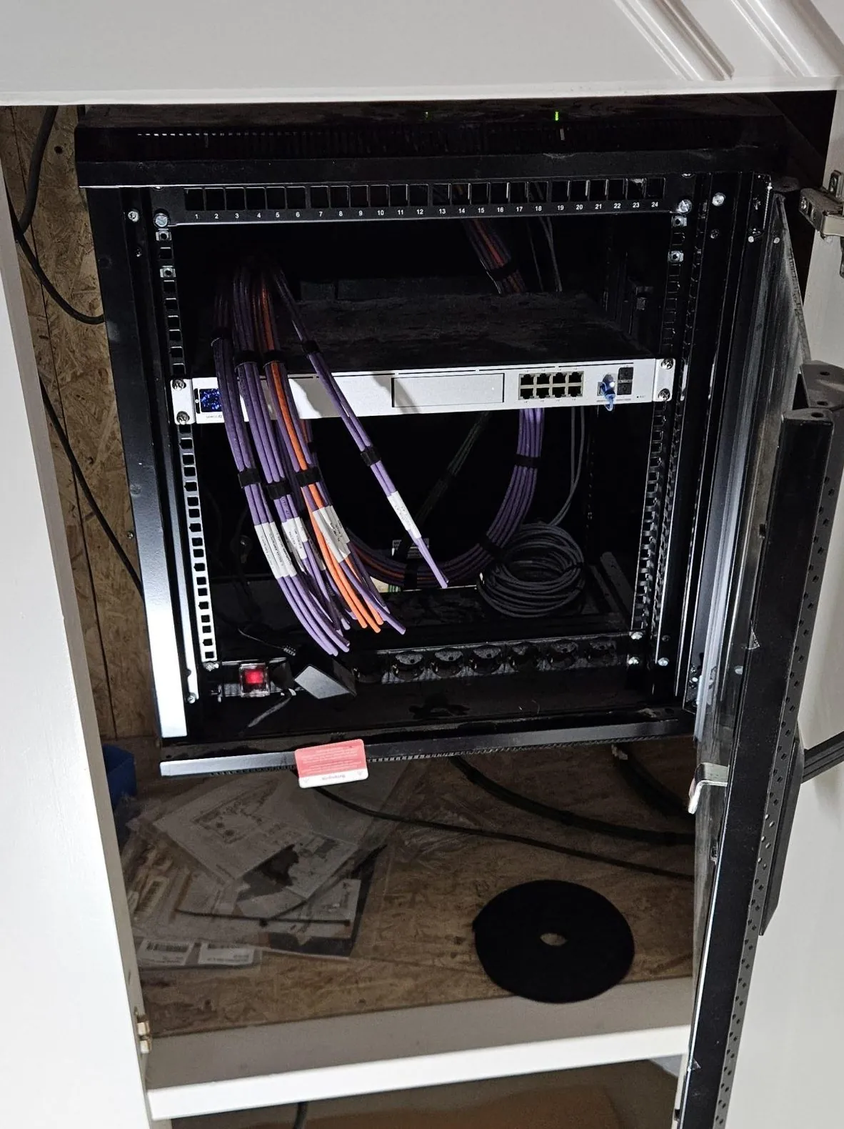 Open netwerkkast in een woning in Amsterdam met een UniFi-switch en opgerolde, gelabelde datakabels