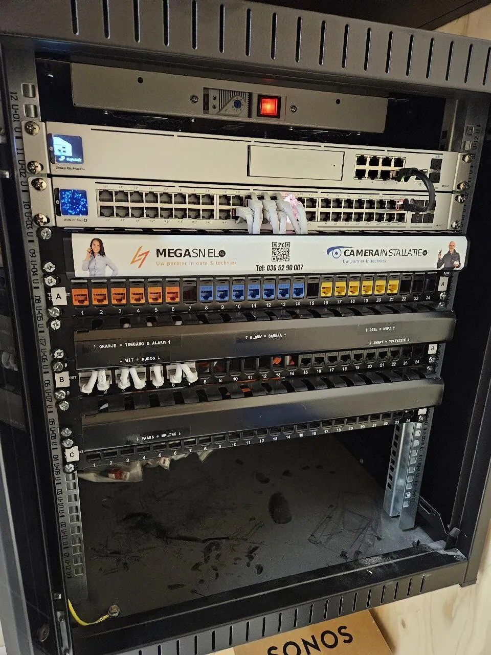 Open netwerkkast in een villa met UniFi-gateway, switch en patchpanelen in oranje, blauw en geel
