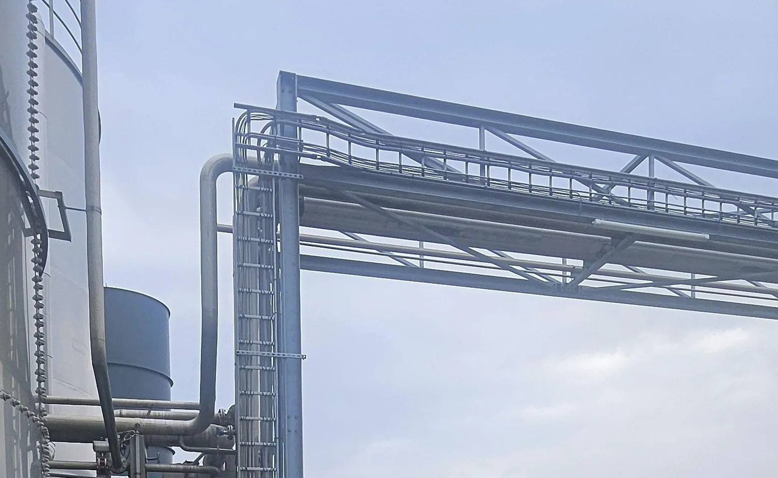 Stalen pijpbrug naast hoge opslagtanks in Amsterdam, met een loopbrug en een ladder