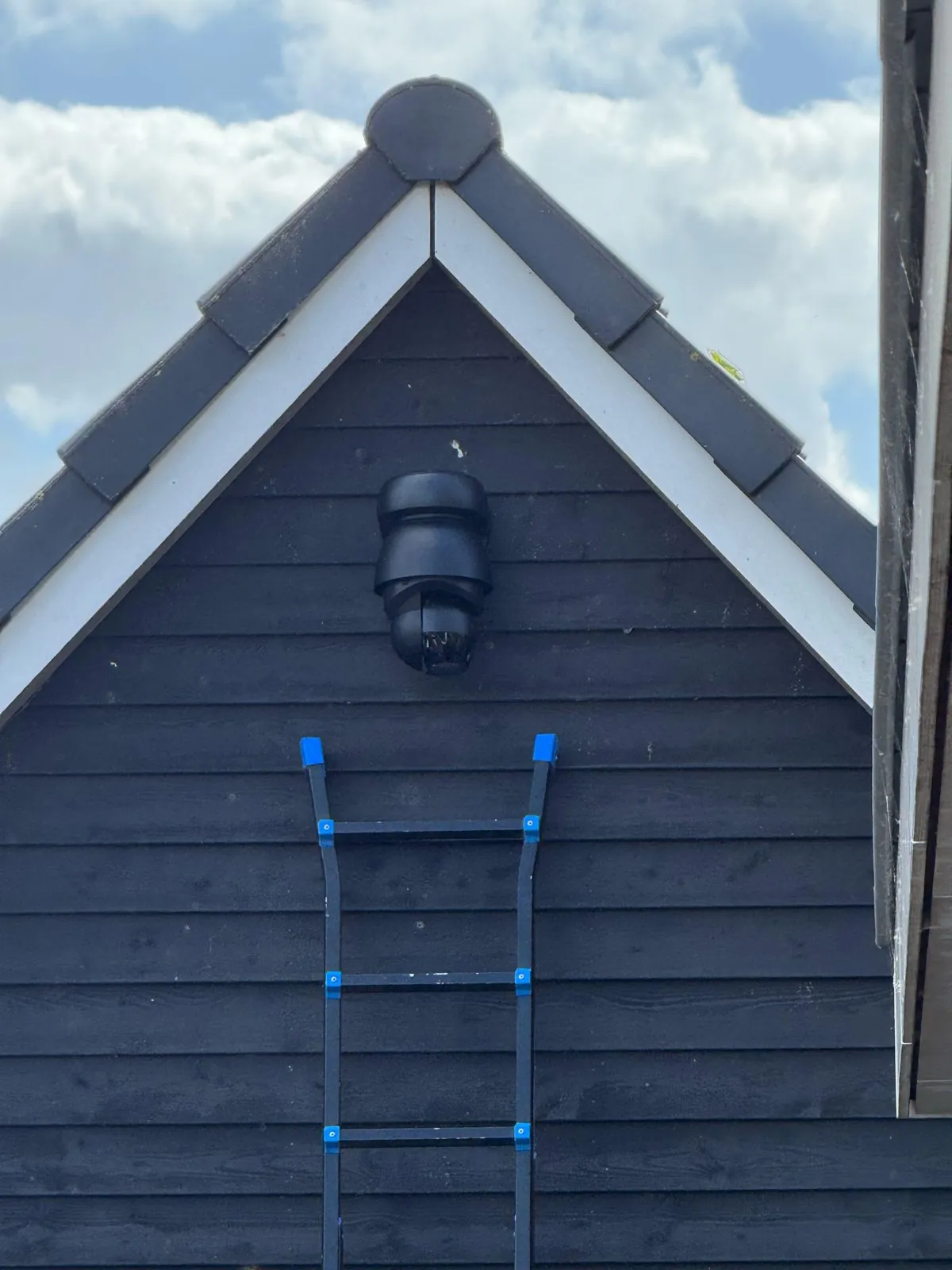 Zwarte PTZ-camera bovenin de schuurnok, tegen het witte boeiboord, in Blaricum