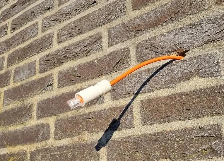 Oranje kabel met RJ45-stekker uit de gevel, klaar voor de camera