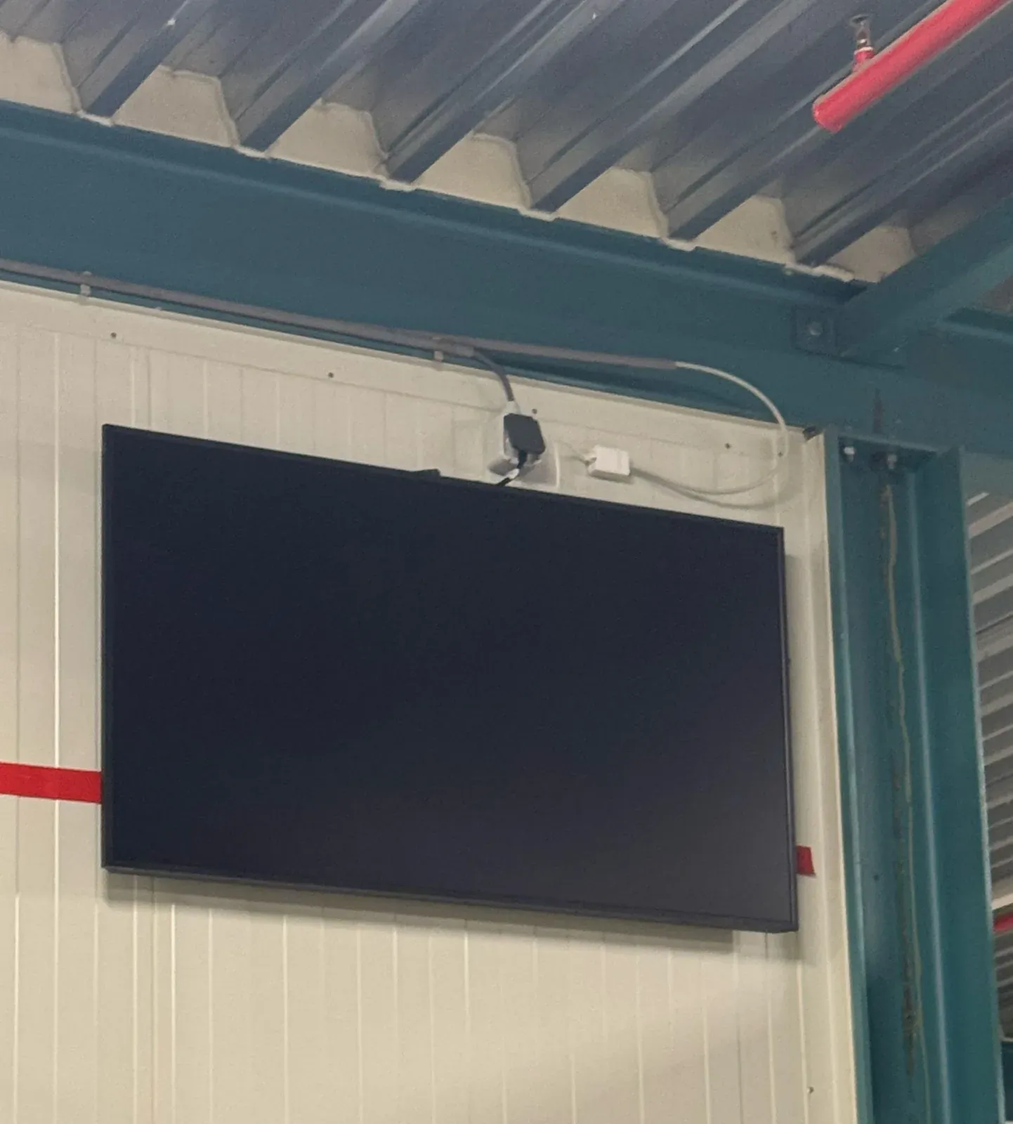 Scherm van 50 inch aan de staalconstructie van een productiehal in Alkmaar, met de kabel strak langs het staal