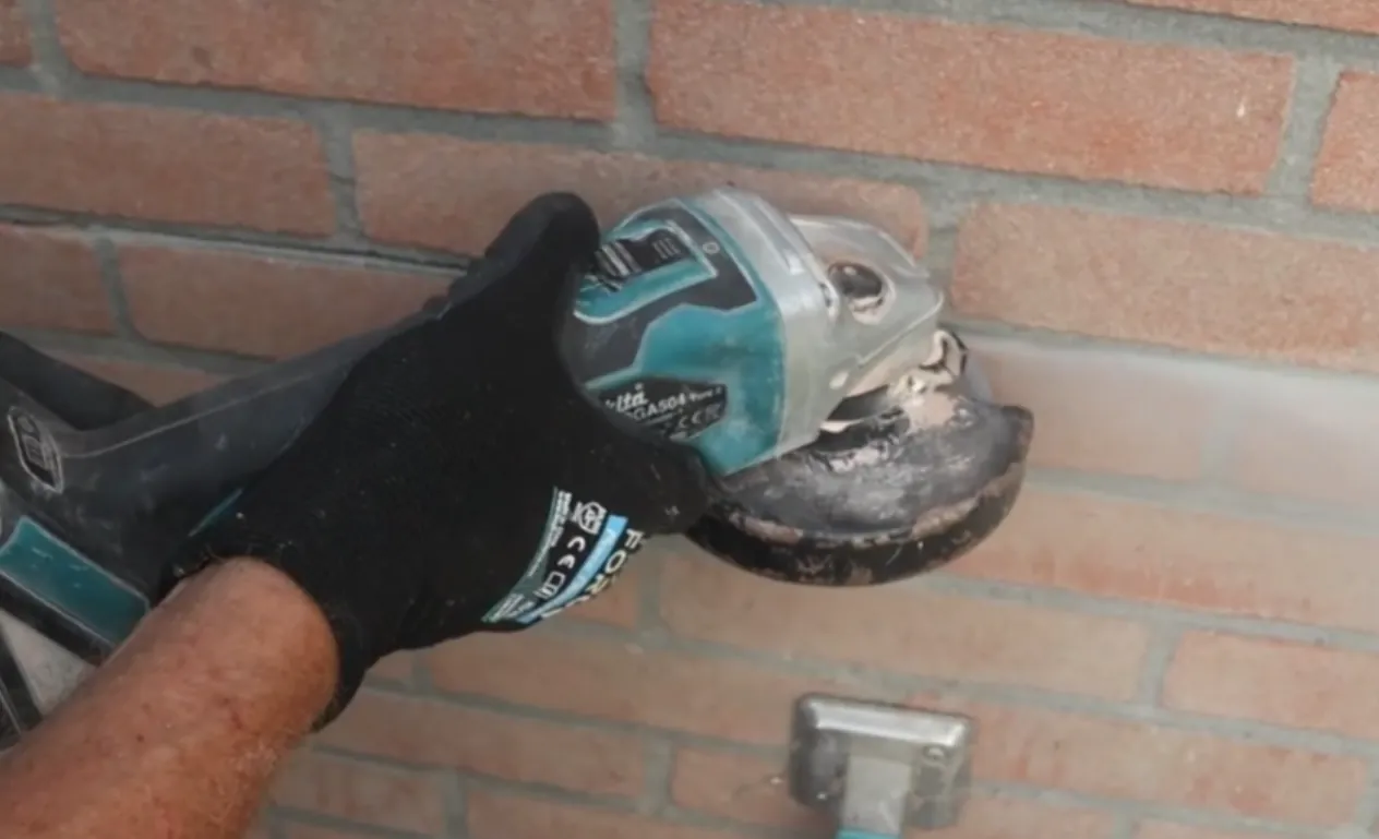 Monteur maakt met de slijptol een smalle sleuf in de liggende voeg van het metselwerk