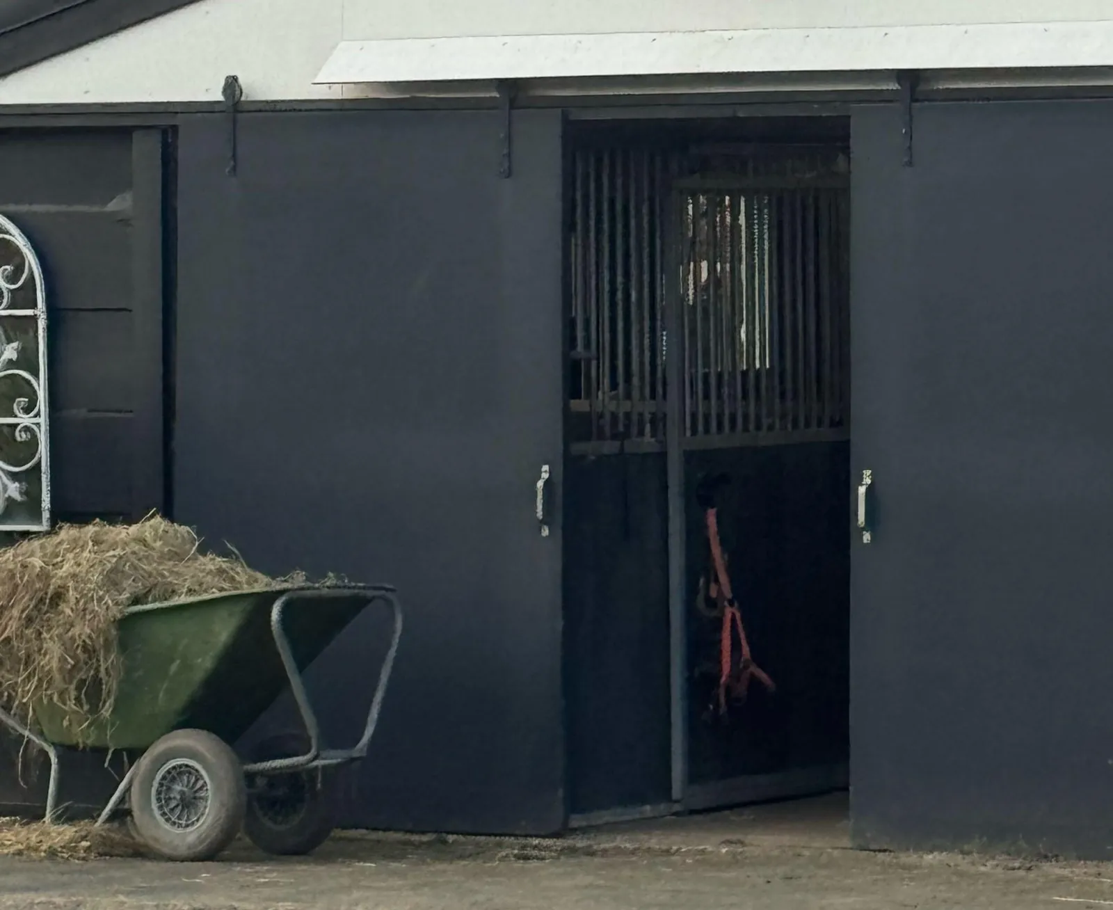 Kruiwagen met hooi voor de geopende staldeur op het erf in Twisk